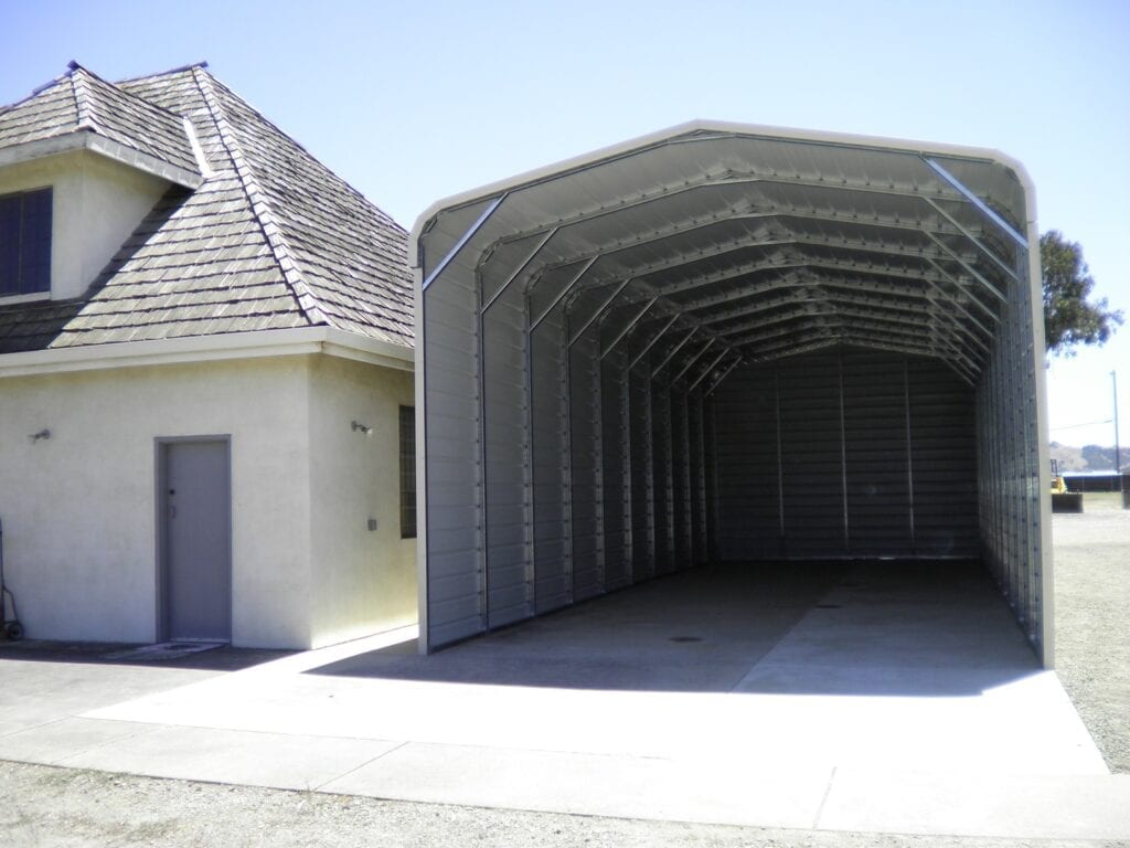 Empty gray metal carport attached to a small white building beside a paved driveway
