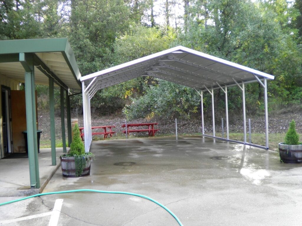 Covered outdoor patio with concrete floor, white canopy, red picnic tables, and potted plants by a building