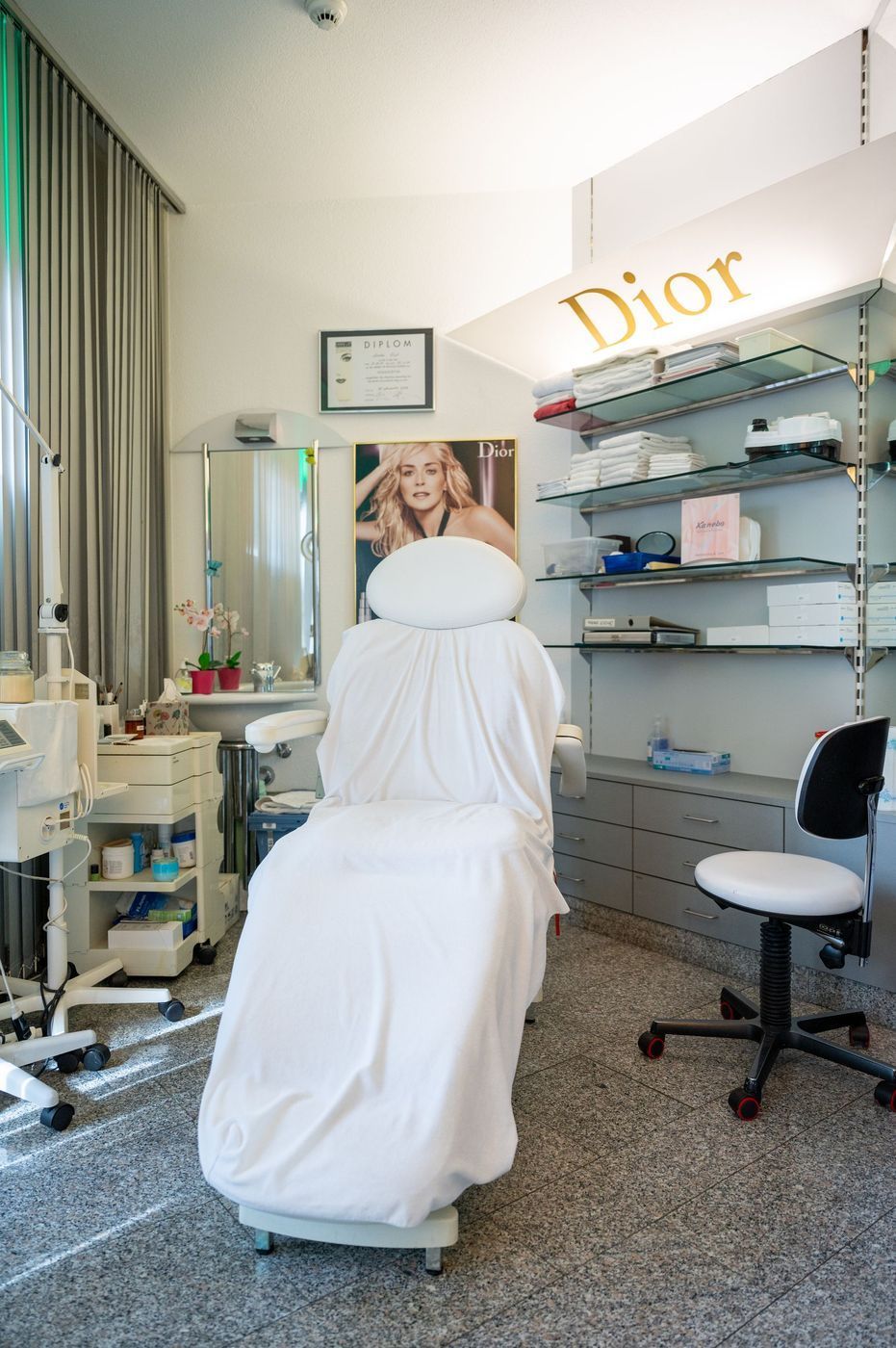 Ein mit Dior-Logo gestalteter Schönheitsbehandlungsraum mit einem weiss bezogenen Stuhl, Regalen und Salonausstattung.