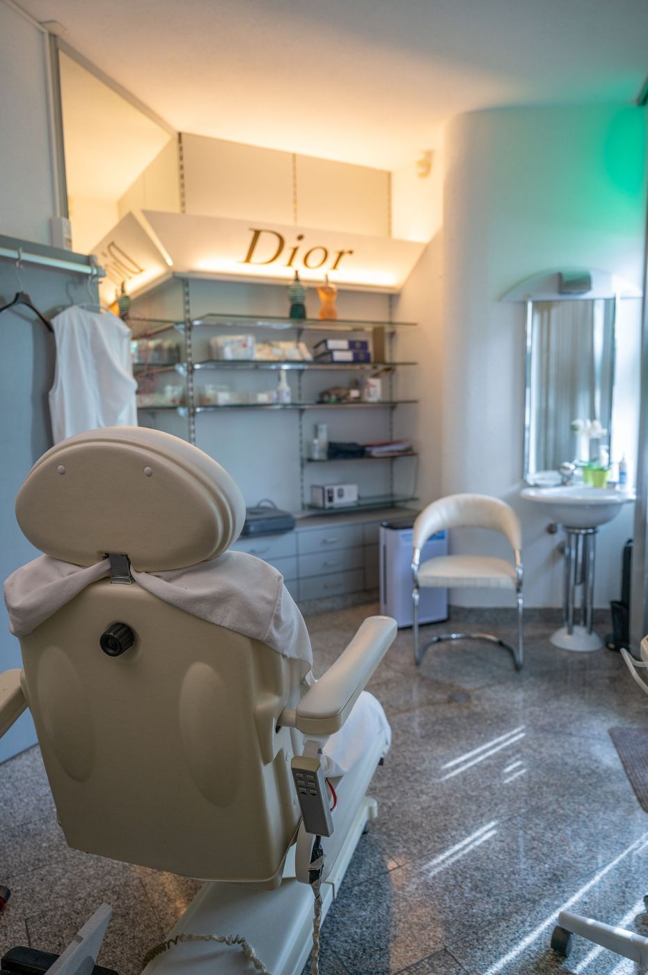 Ein Schönheitssalon mit einem cremefarbenen Gesichtsbehandlungsstuhl, Regalen, Spiegel und einem leuchtenden Dior-Schild.