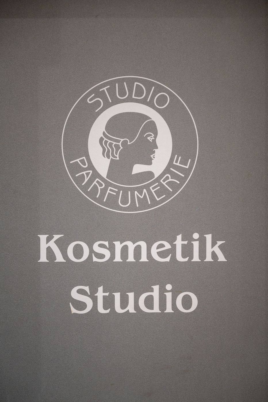 Schild eines Kosmetikstudios mit kreisförmigem „Studio Parfümerie“-Logo an einer dunklen Wand