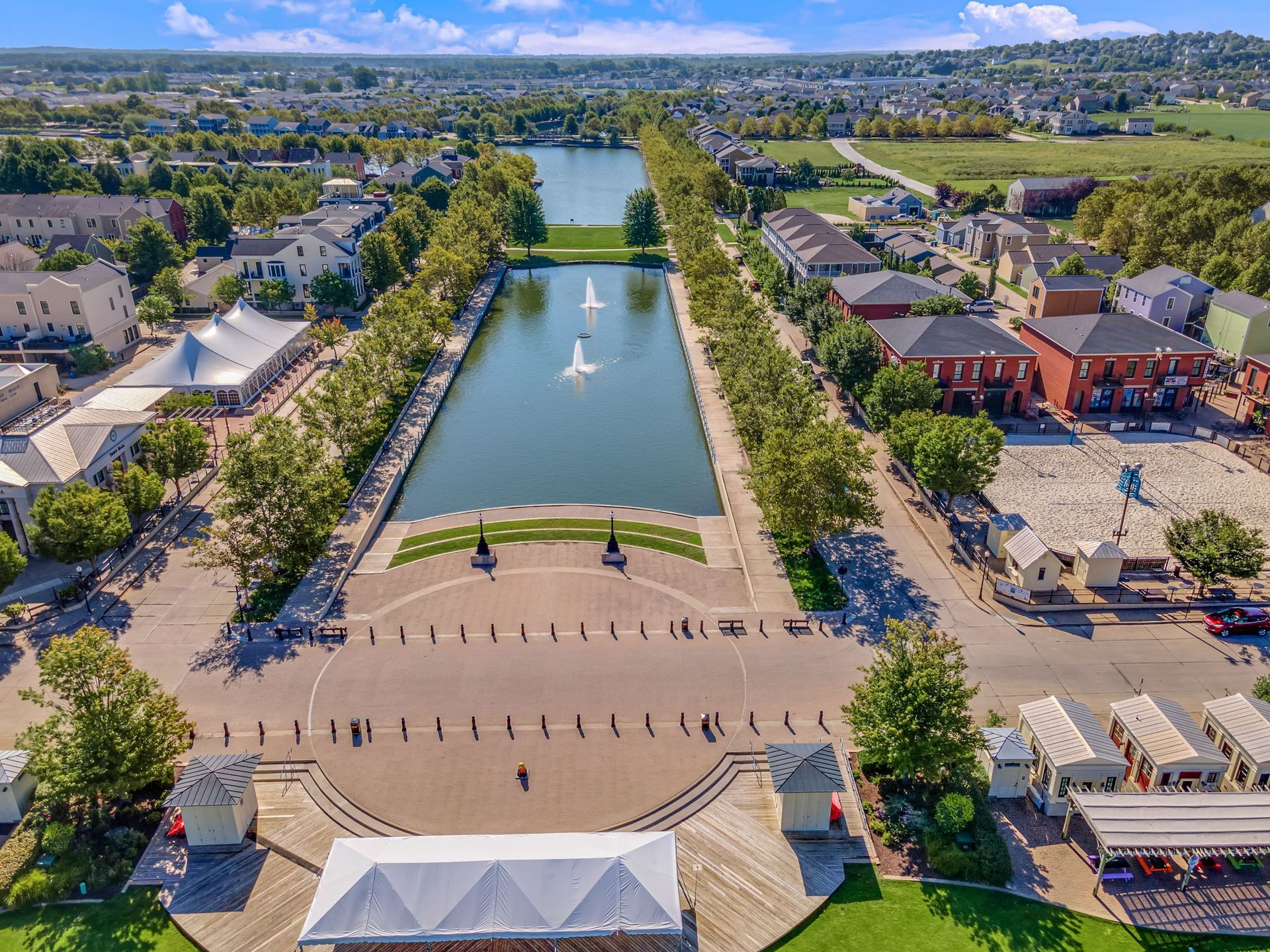 Aerial view of a long reflecting pool and fountain in a landscaped plaza with surrounding buildings and hills.