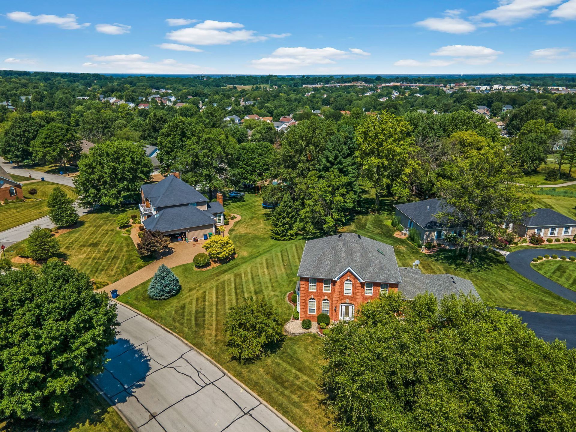Aerial view of a suburban neighborhood with brick houses, green lawns, and tree-lined streets.