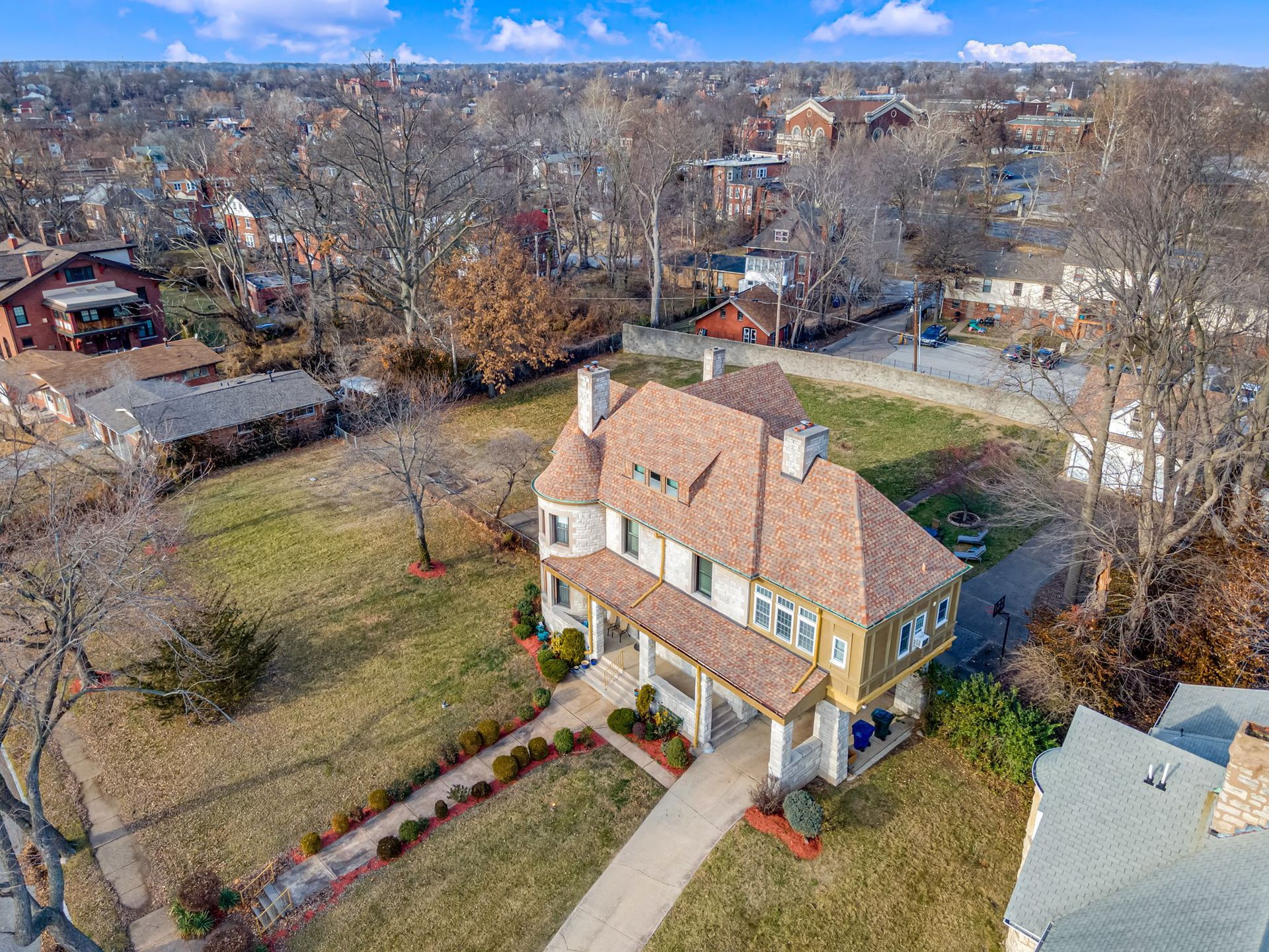 Aerial view of a two-story beige house with a red roof and front porch in a suburban neighborhood.