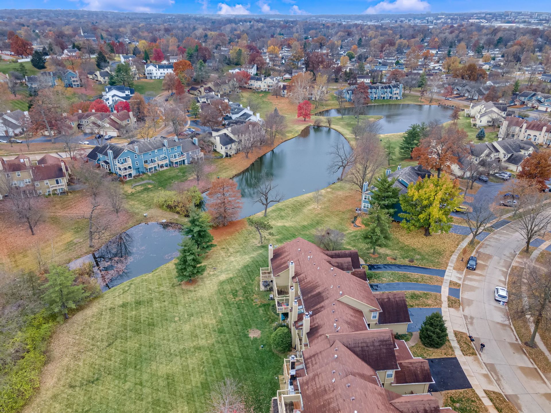 Aerial view of a suburban neighborhood with a pond, autumn trees, and roads.