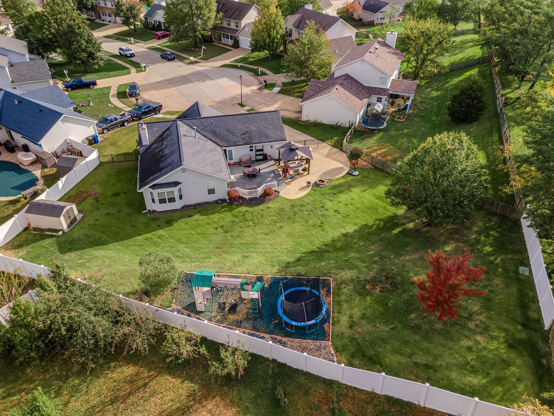 Aerial view of a suburban neighborhood with houses, driveways, lawns, and a backyard trampoline.