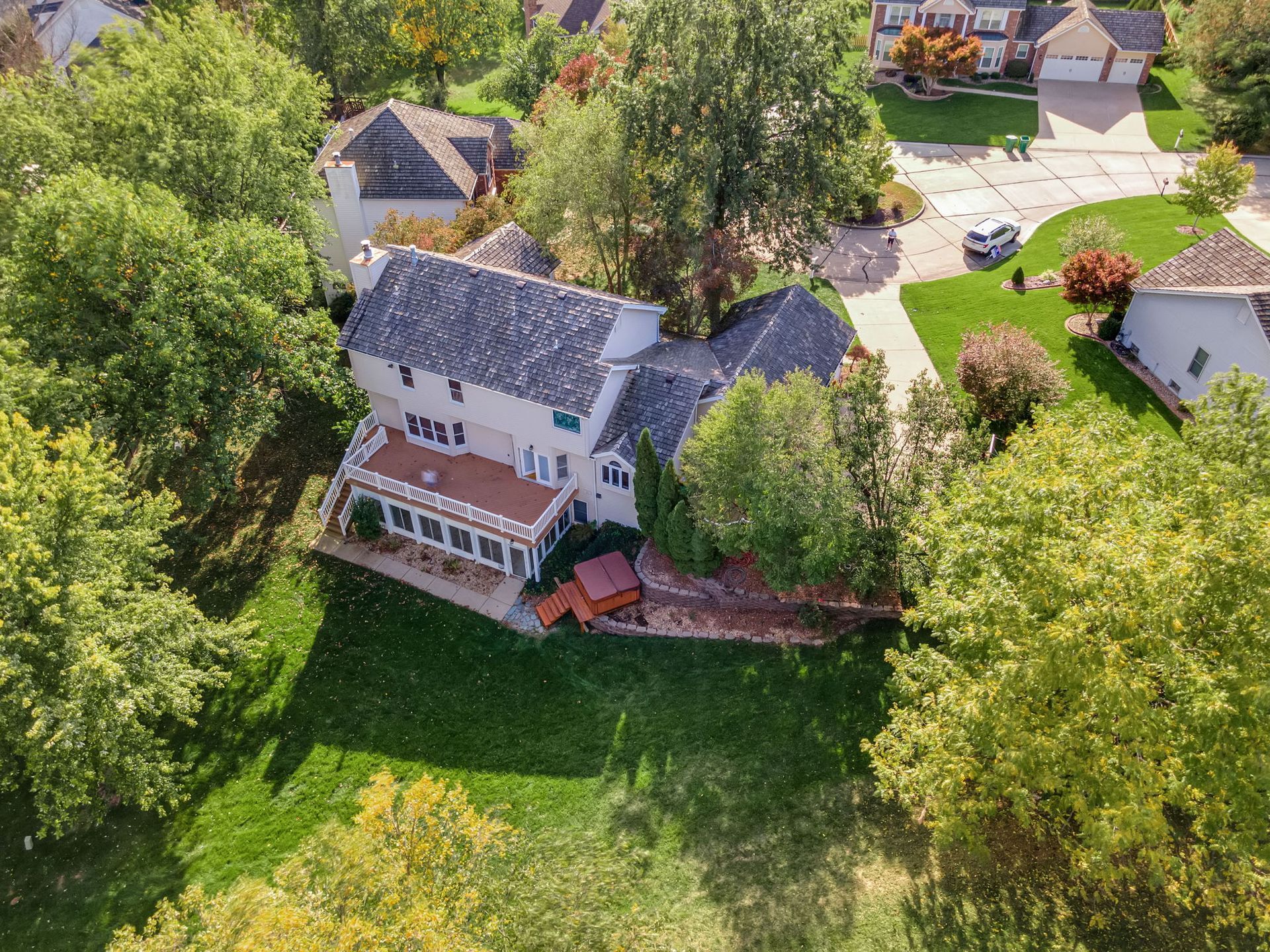 Aerial view of a pink house with a gray roof surrounded by trees and a green lawn.