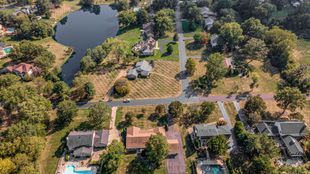 Aerial view of a suburban neighborhood with homes, trees, roads, and a small pond