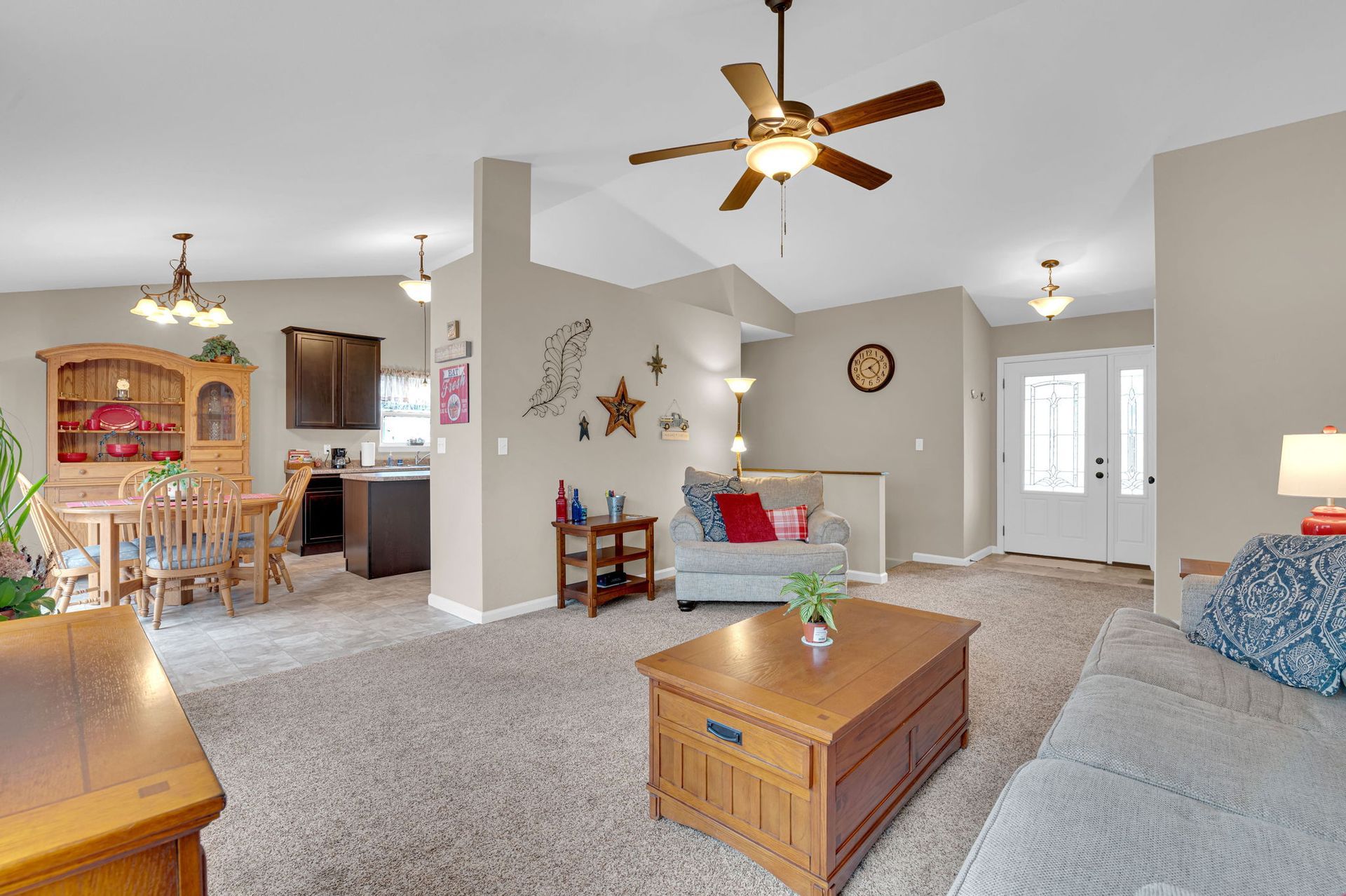 Bright living room with carpet, ceiling fans, couch, coffee table, and open dining area/kitchen.
