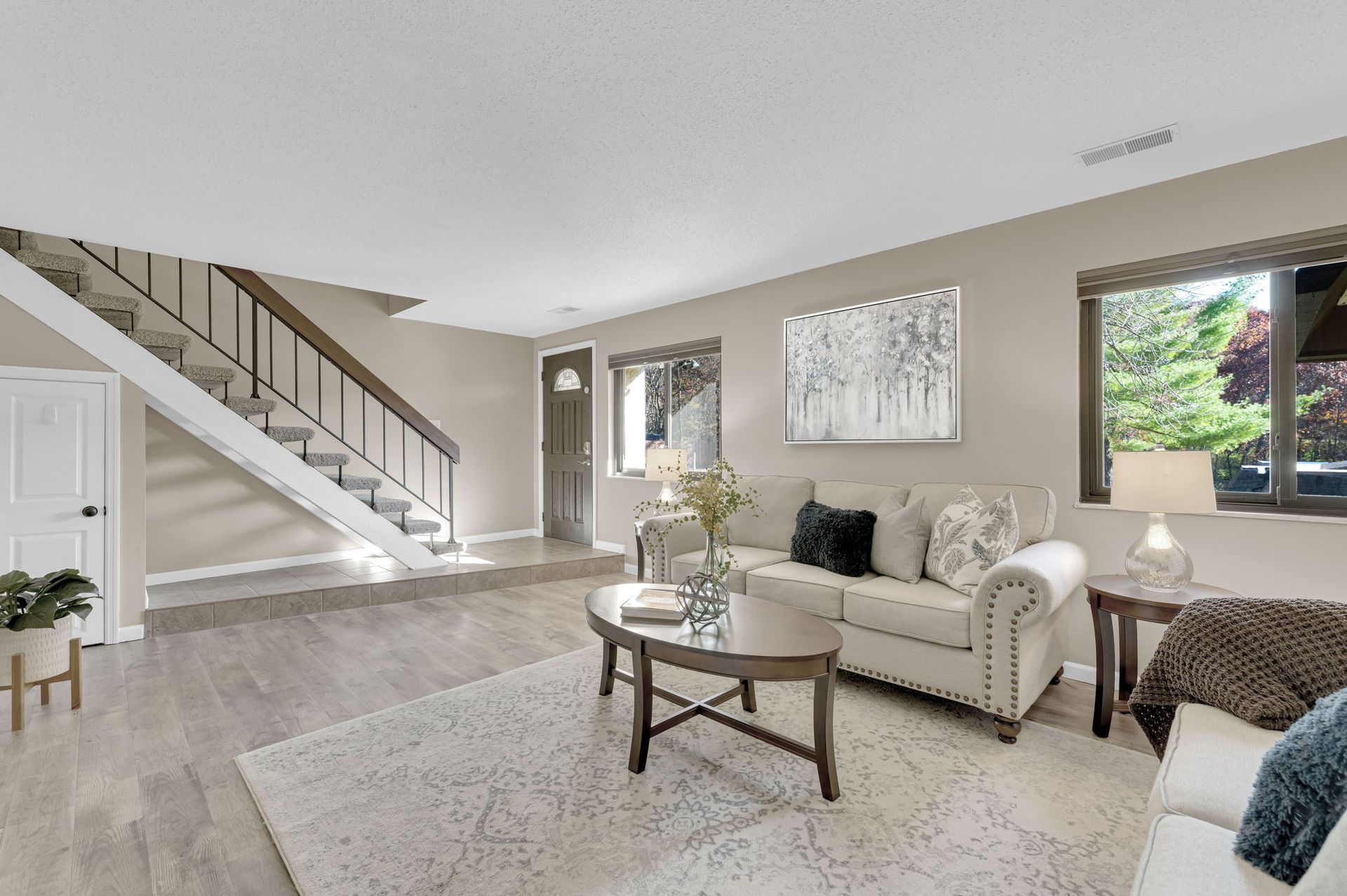 Bright living room with white sofa, staircase, and large windows overlooking greenery