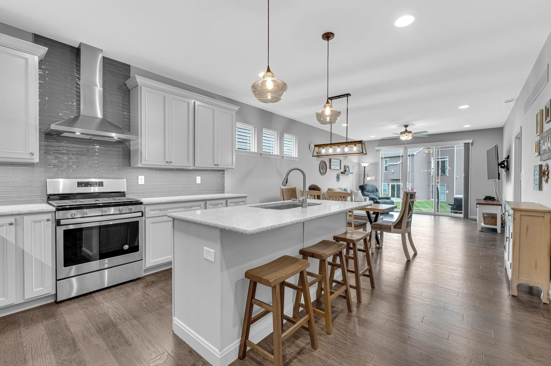 Bright open kitchen with white cabinets, stainless stove, island stools, and hardwood floors in a modern home