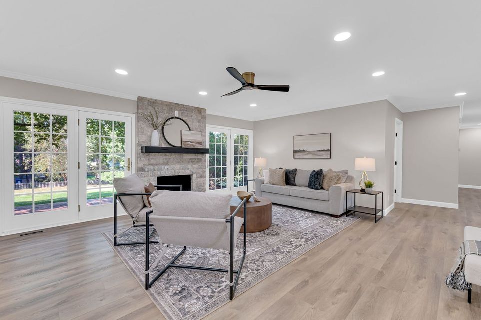 Bright open living room with stone fireplace, gray sofas, dining table, and large windows overlooking a pool.