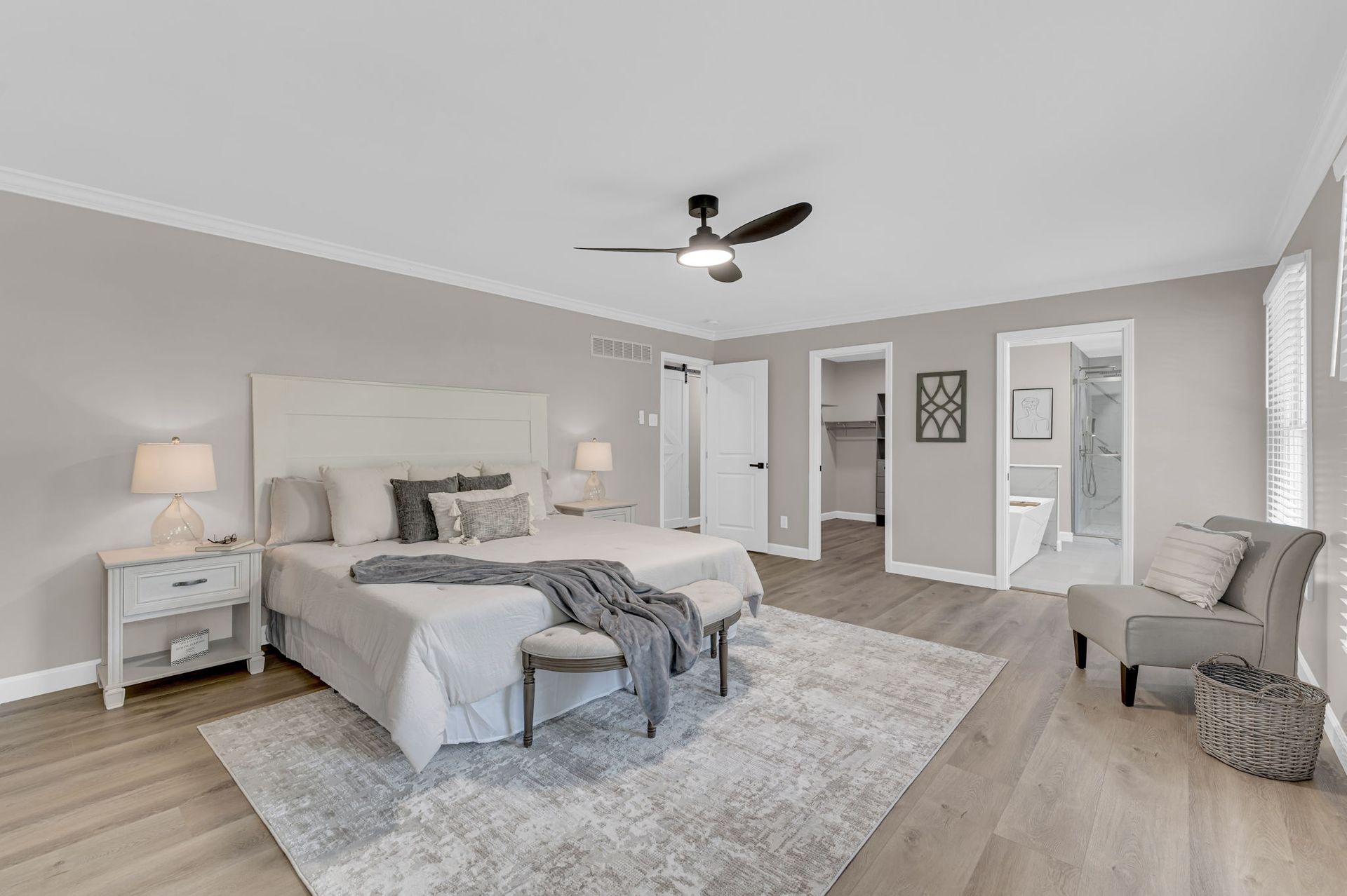 Spacious gray bedroom with a king bed, nightstand, chair, and large rug, seen in soft neutral tones