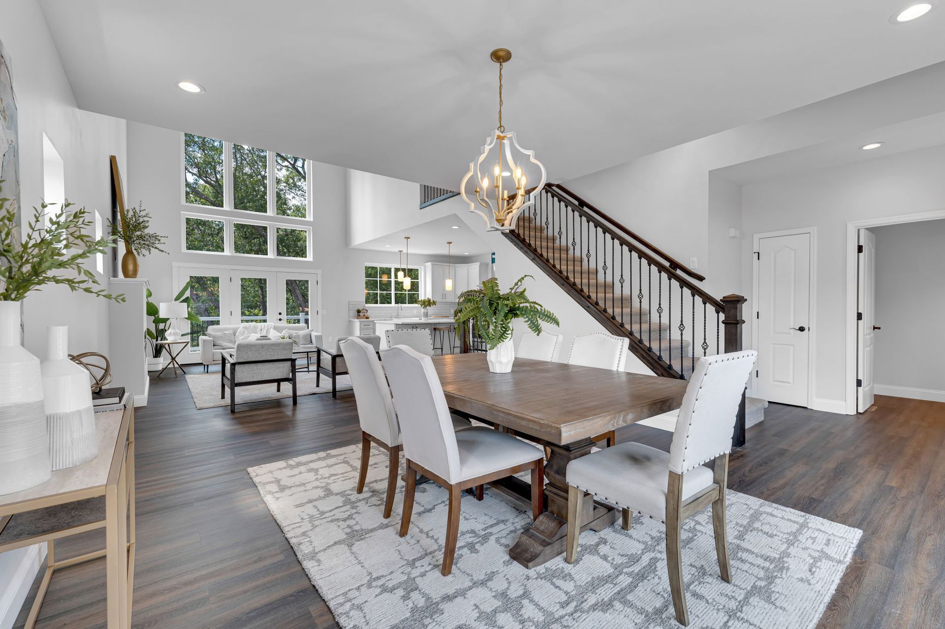 Bright open dining room with wooden table, white chairs, staircase, and large windows