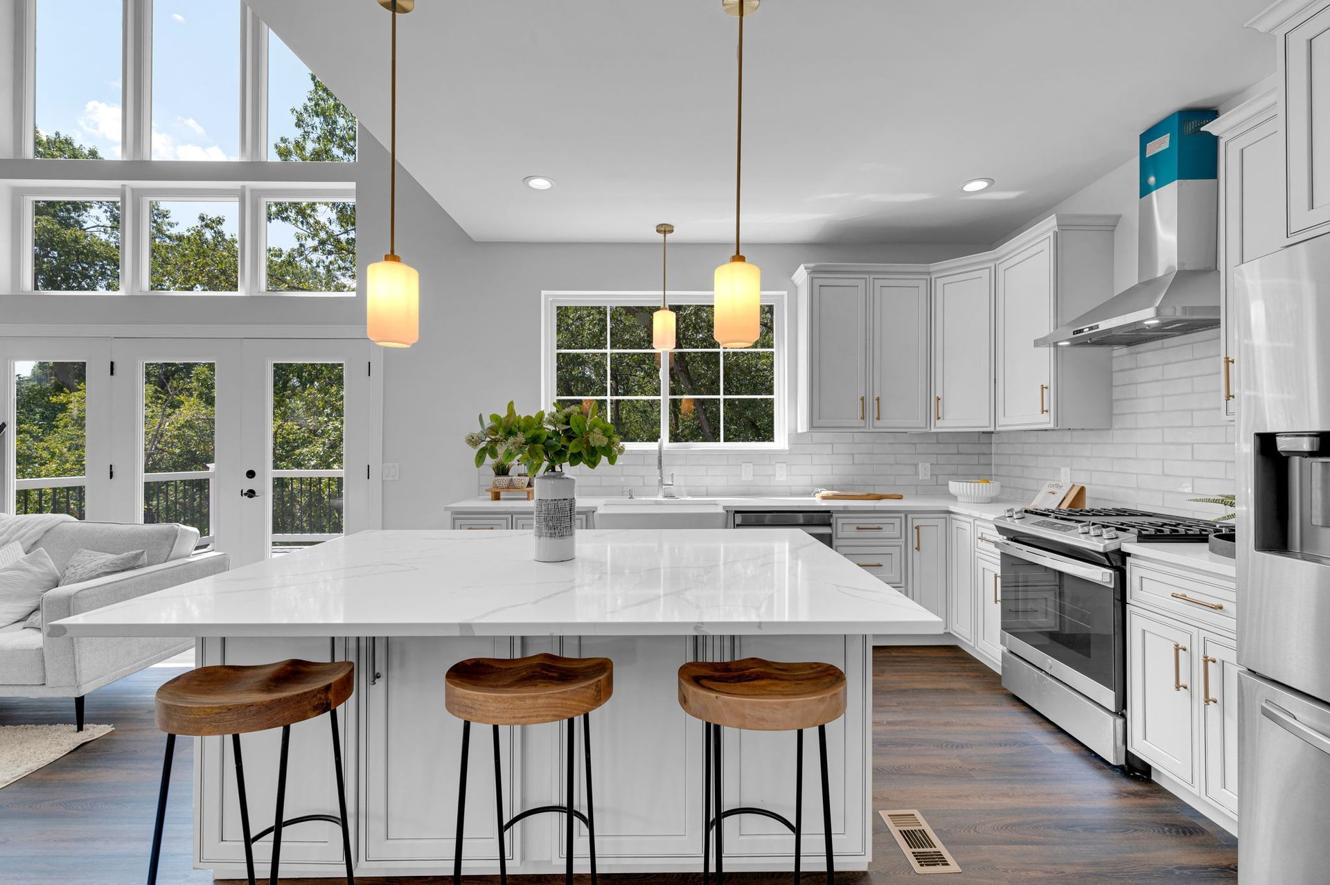 Bright modern kitchen with white cabinets, island seating, pendant lights, and large windows