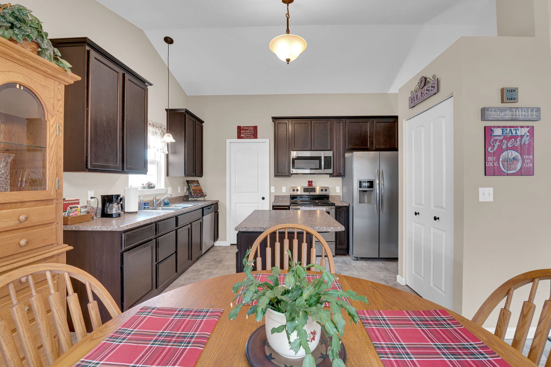 Dining area and kitchen with dark wood cabinets, stainless appliances, and a wooden table with red plaid placemats