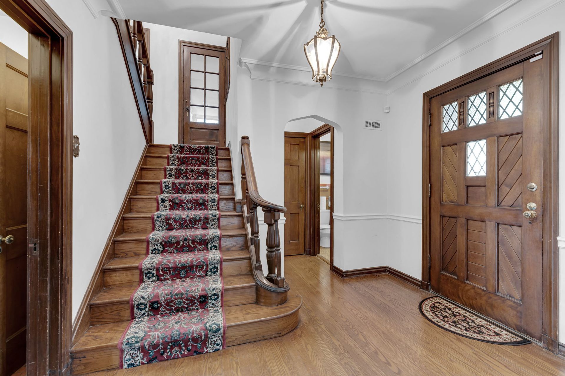 Front entry hall with wooden stairs, patterned runner, wood floor, and front door with glass panels
