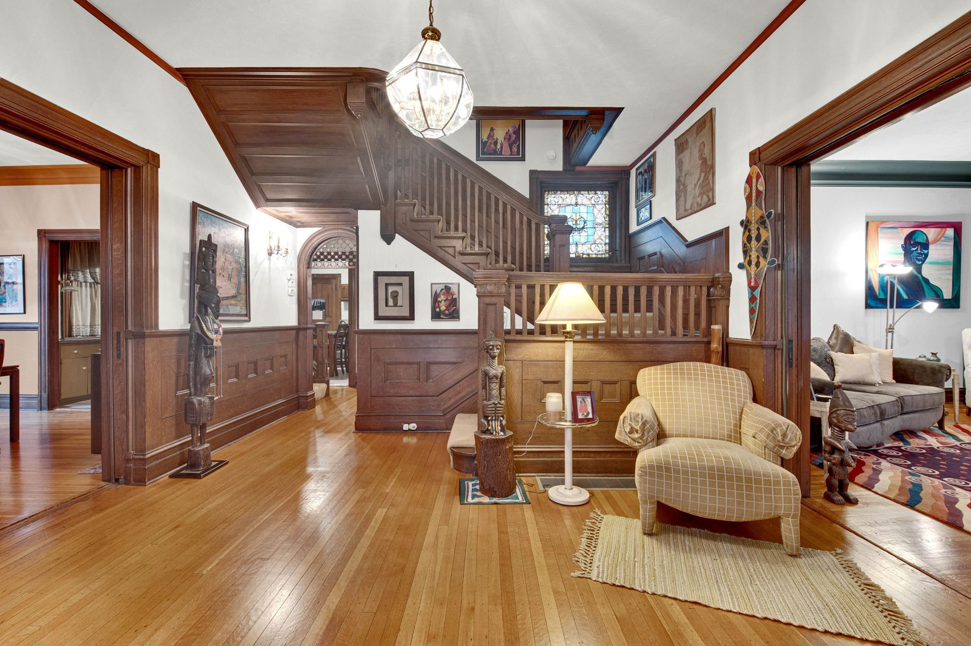 Bright foyer with hardwood floors, staircase, beige chair, and framed art in a home interior.