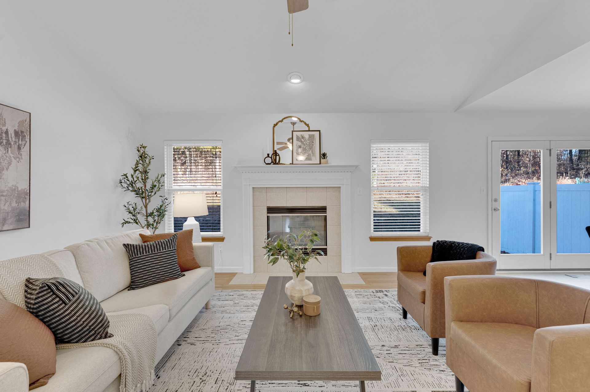 Bright modern living room with white sofa, fireplace, tan chairs, and blue-patio views