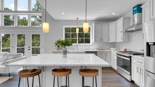Bright modern kitchen with white cabinets, island seating, pendant lights, and large windows