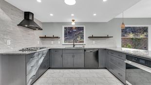 Modern gray kitchen with white tile backsplash, stainless appliances, and black range hood