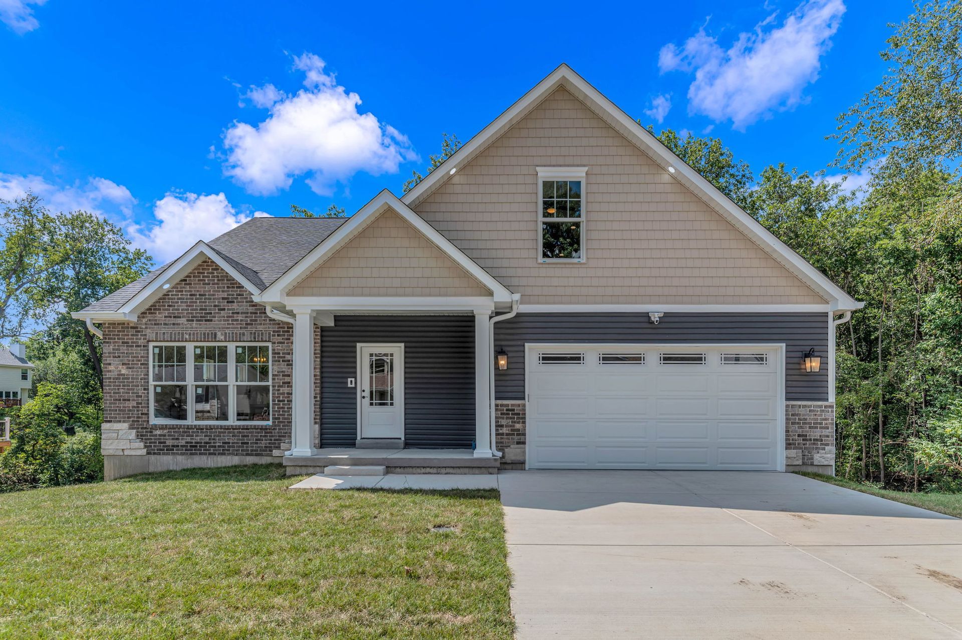 Single-story beige house with front porch, two-car garage, and green lawn under a blue sky.