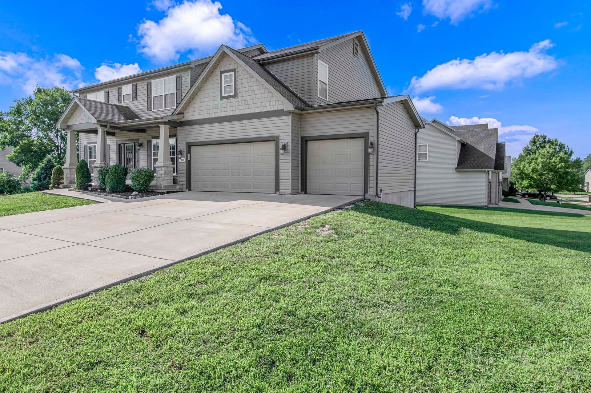 Suburban house with three-car garage, large driveway, and green lawn under a blue sky