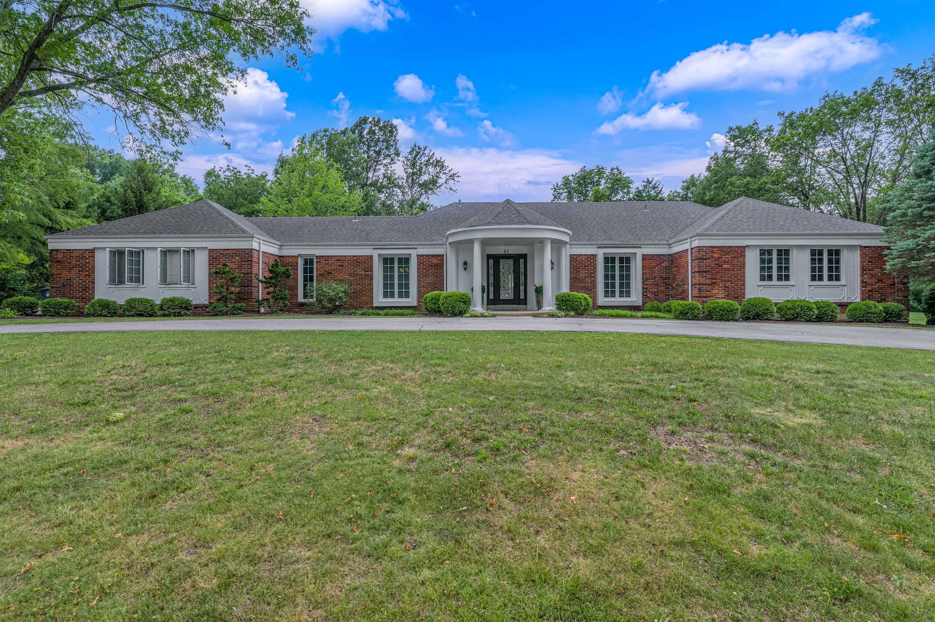 Single-story brick house with white columns, large front lawn, and blue sky