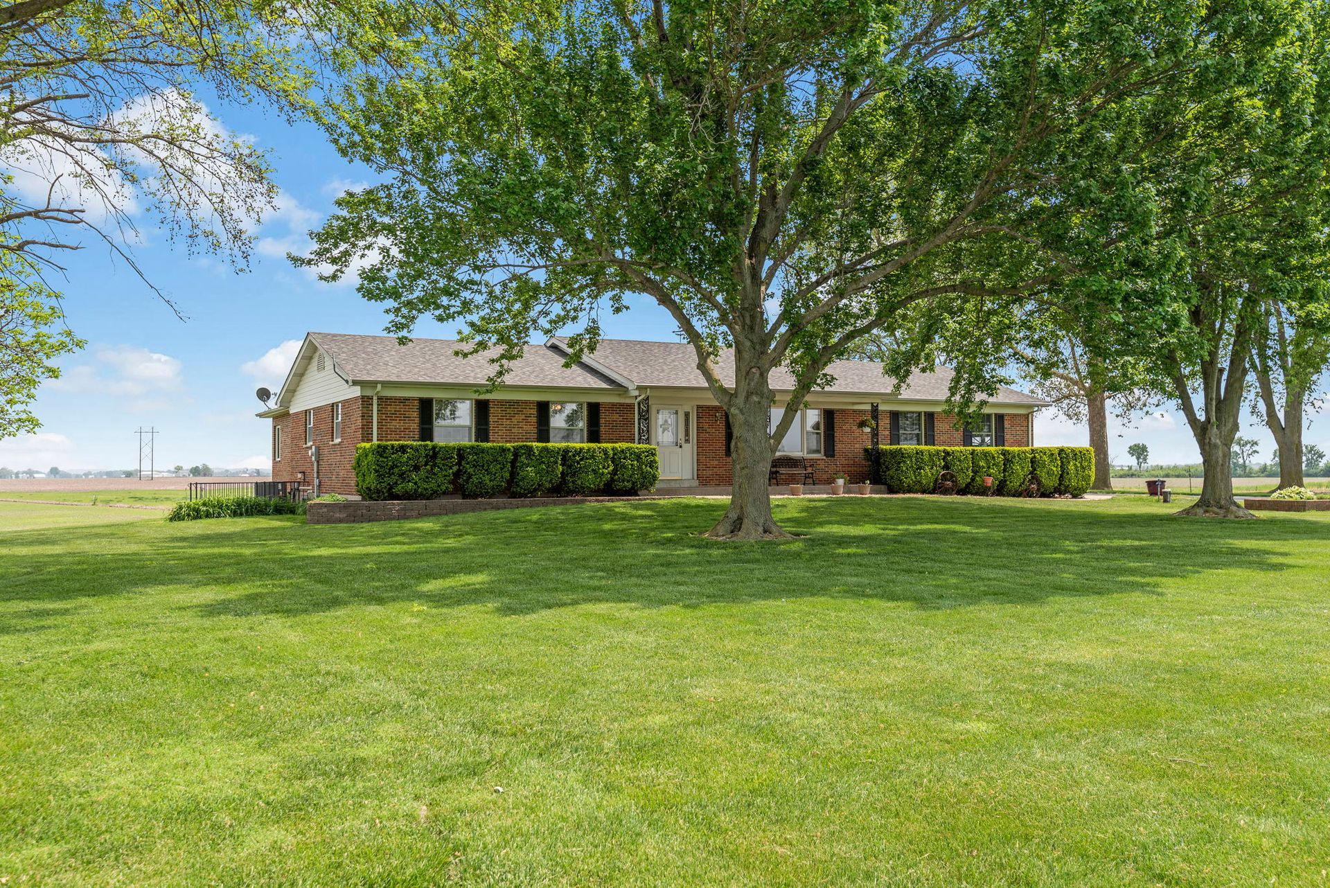 Brick ranch house with a covered porch, trees, and a large green lawn under a bright blue sky