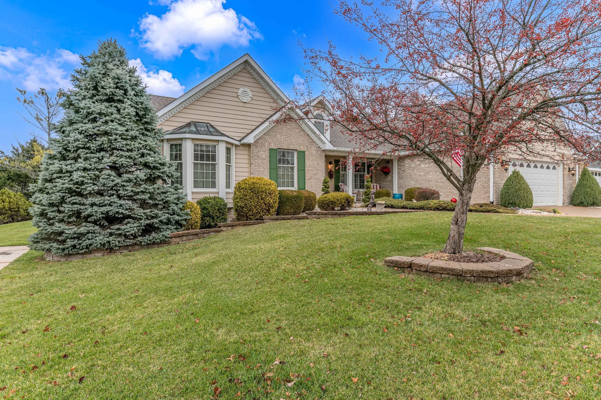 Suburban house with stone facade, green lawn, evergreen tree, and pink flowering tree in front yard