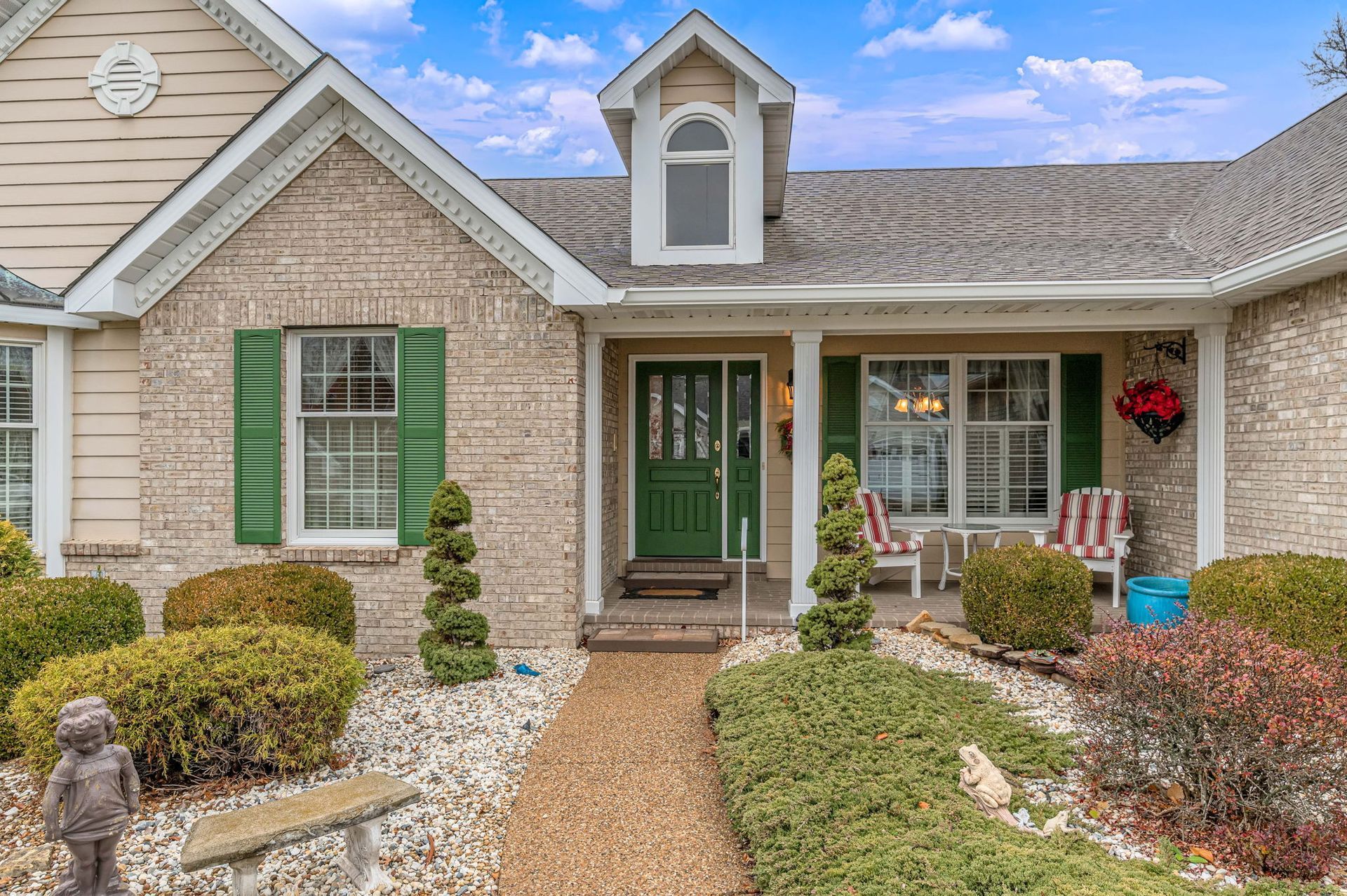 Front view of a brick house with green shutters, a green front door, and a landscaped walkway.