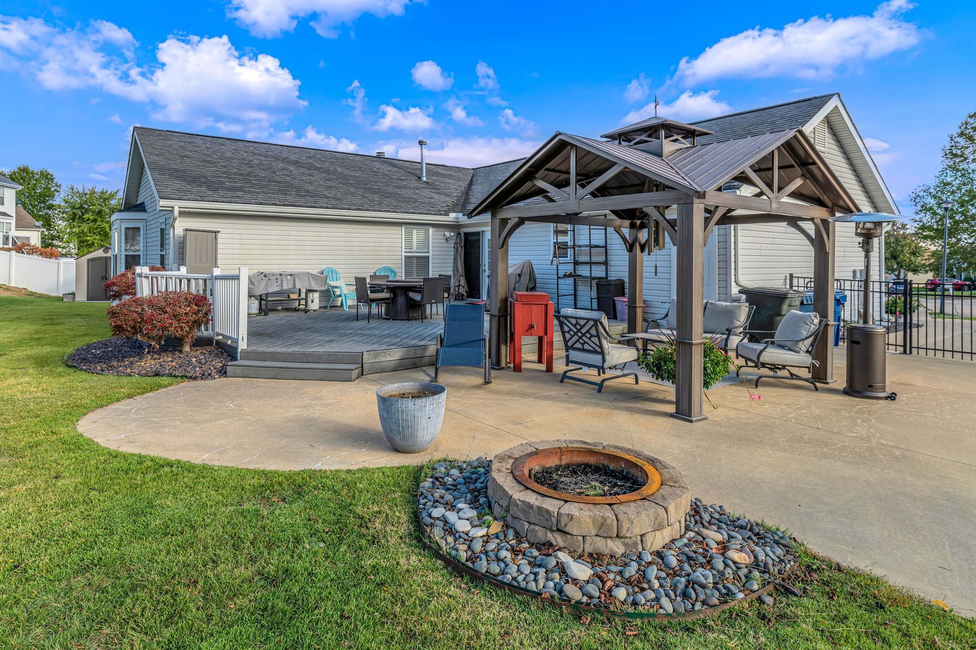 Backyard patio with a covered pergola, fire pit, outdoor seating, and grill beside a house