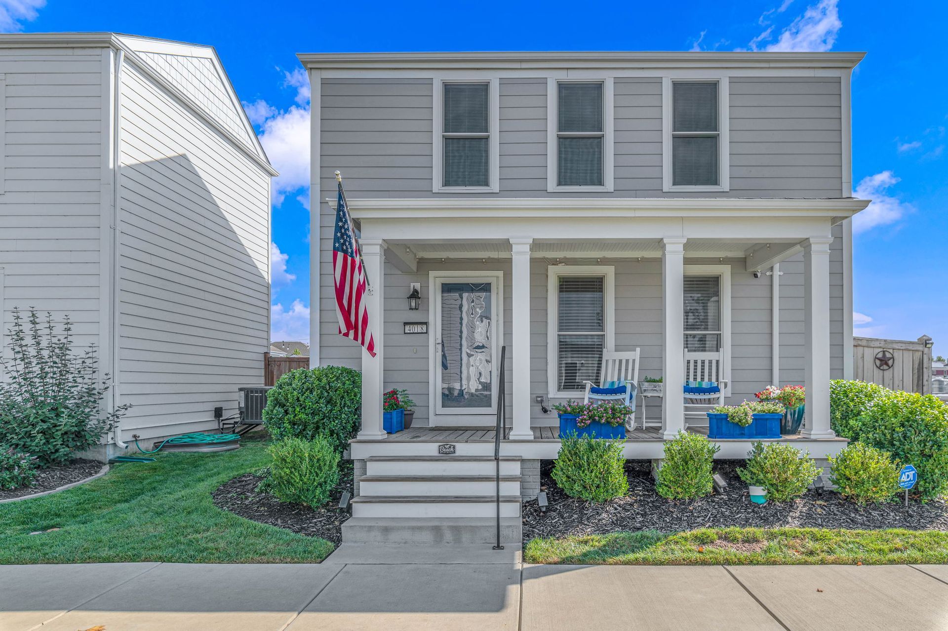 Gray two-story house with a front porch, American flag, and neatly landscaped yard