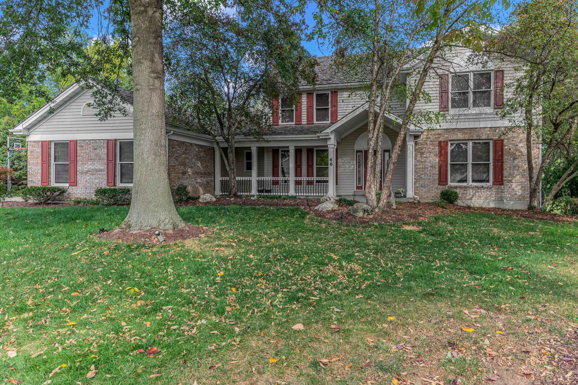 Large two-story stone house with red shutters and a front porch, framed by trees and a grassy yard