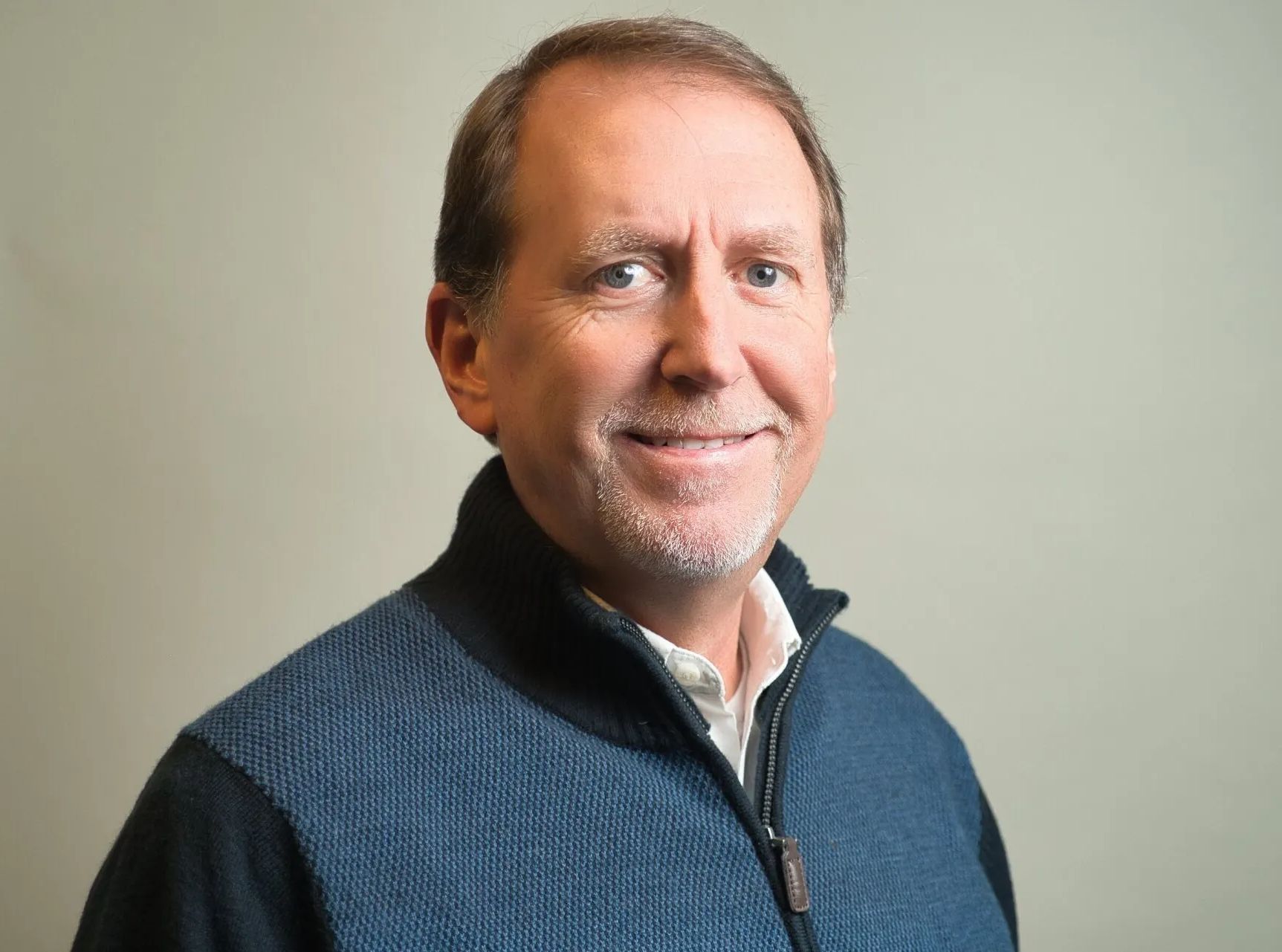 Portrait of a smiling man in a blue sweater against a plain light background