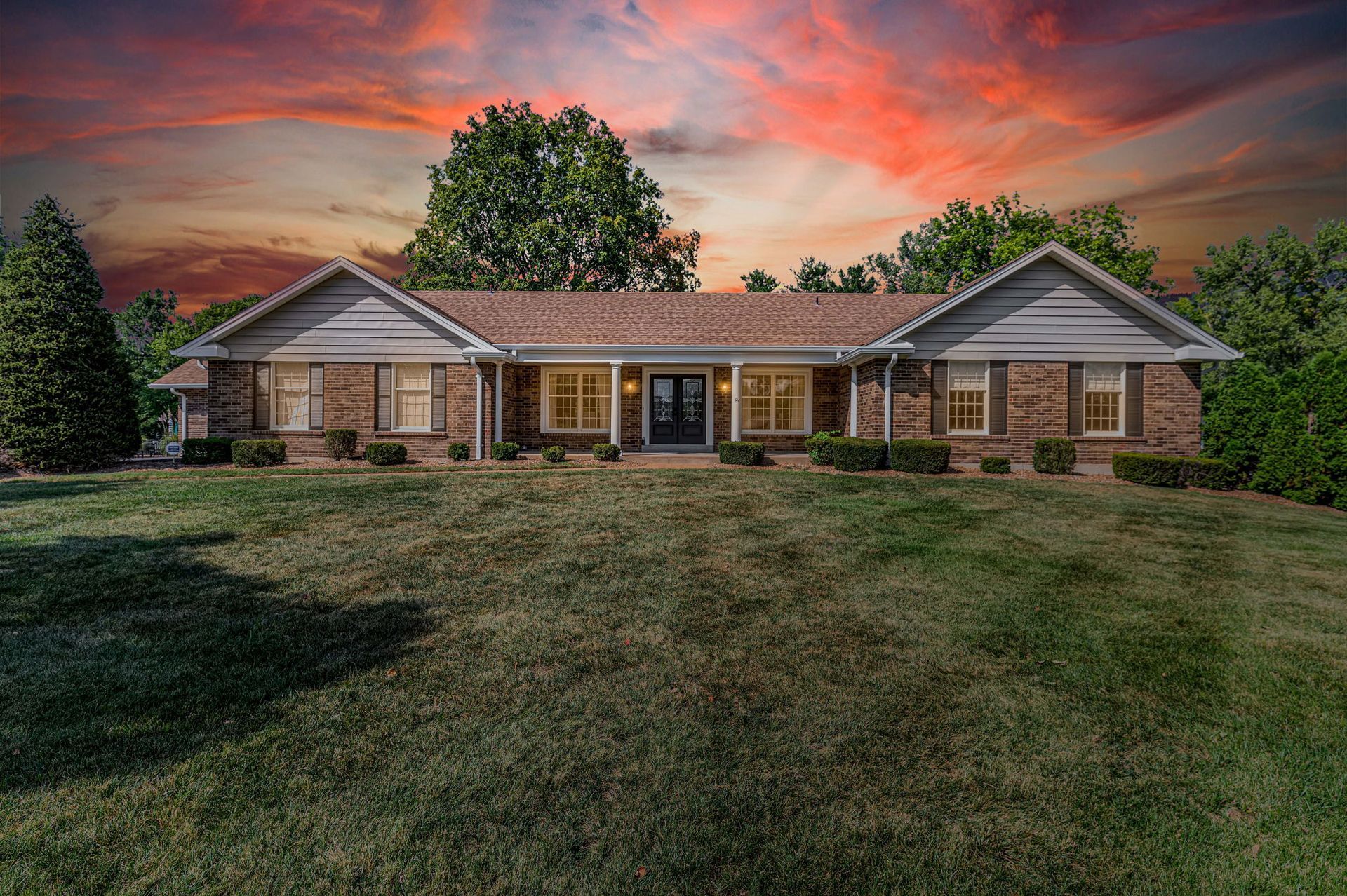 Single-story brick house with a front lawn at sunset under a dramatic pink-orange sky