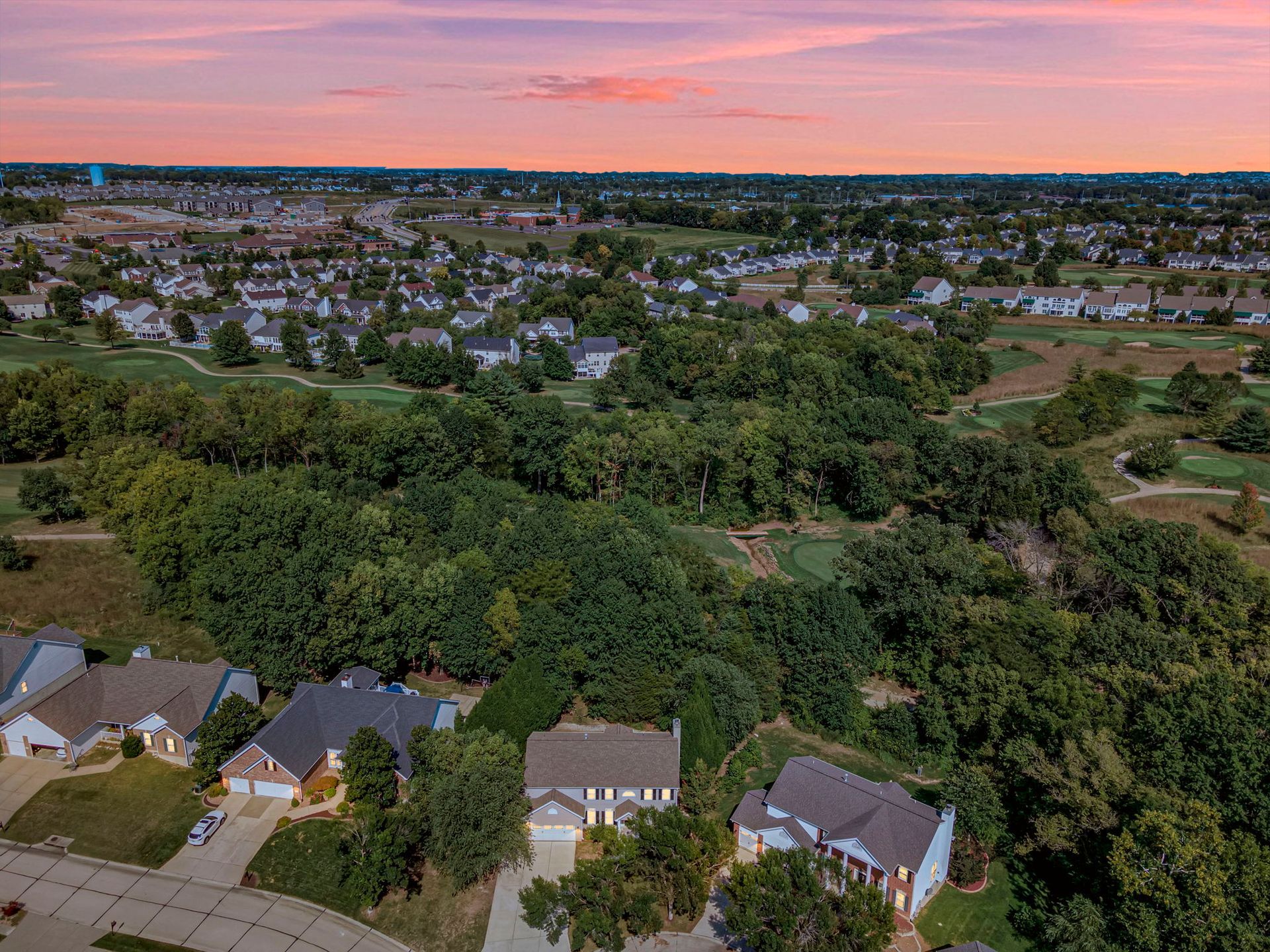 Suburban neighborhood at sunset with rooftops, trees, and a pink-orange sky