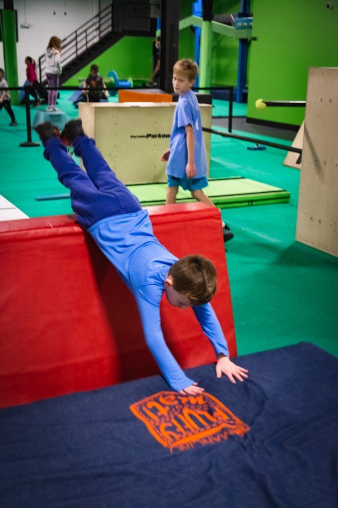 Child doing handstand or flip on red padded obstacle with blue mat