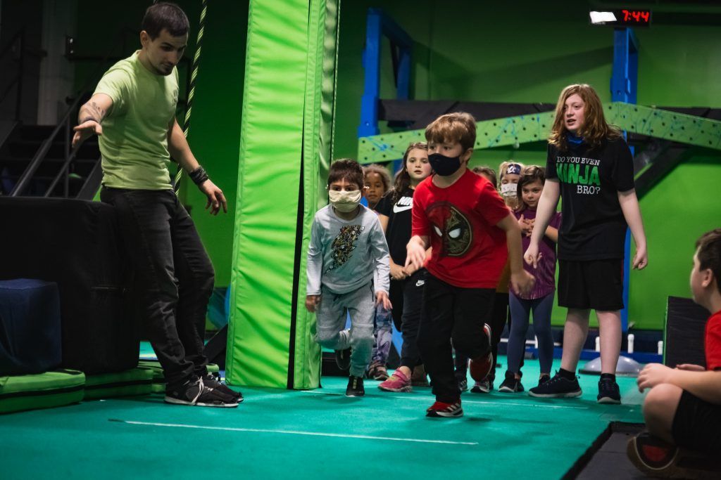 Instructor demonstrating technique to group of young children on green padded floor