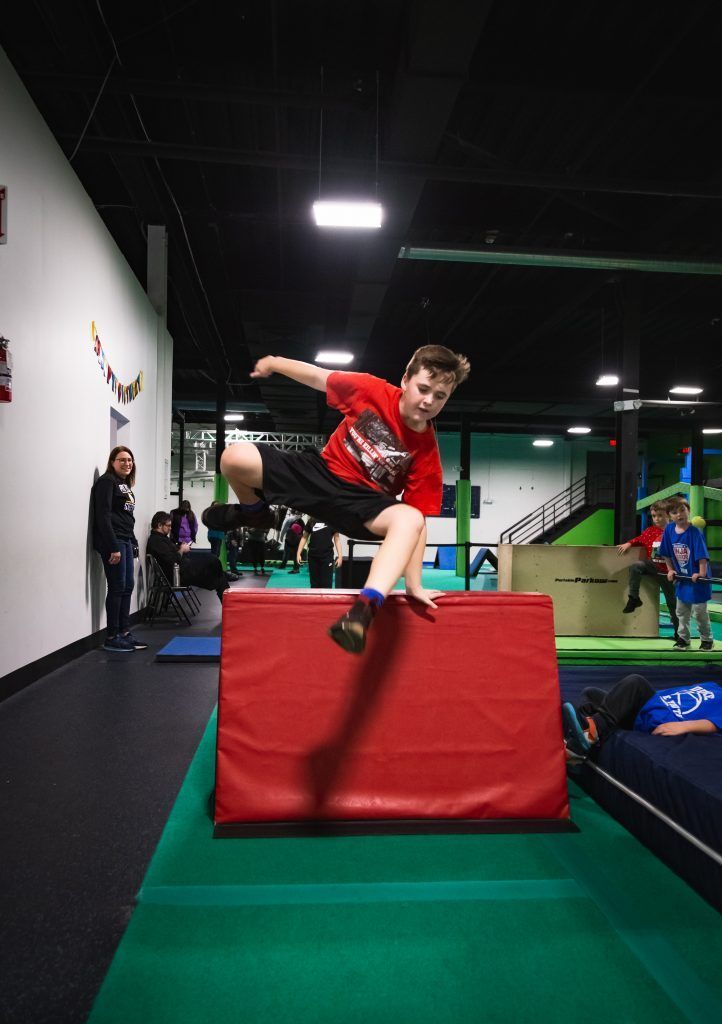 Young athlete jumping over red padded obstacle block during training