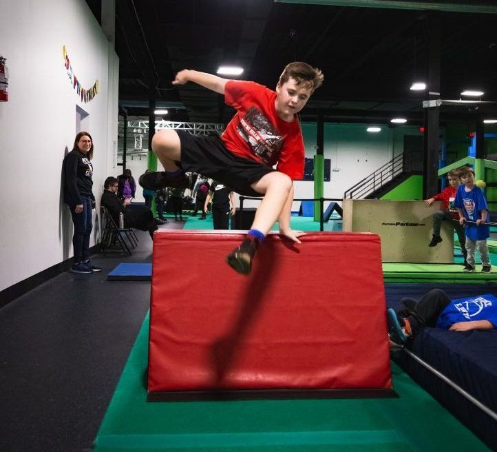 Young athlete jumping over red padded obstacle during ninja warrior training