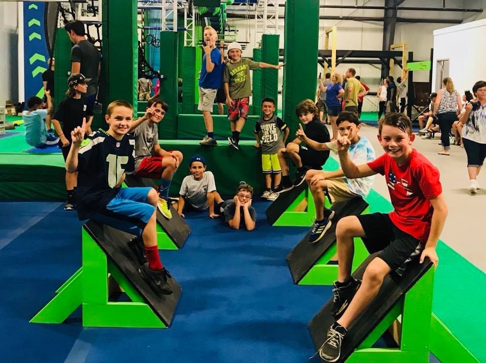 Children in action on angled ninja course obstacles with instructor supervising