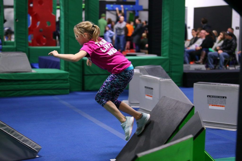 Young girl jumping between angled ninja obstacles on blue and green mats