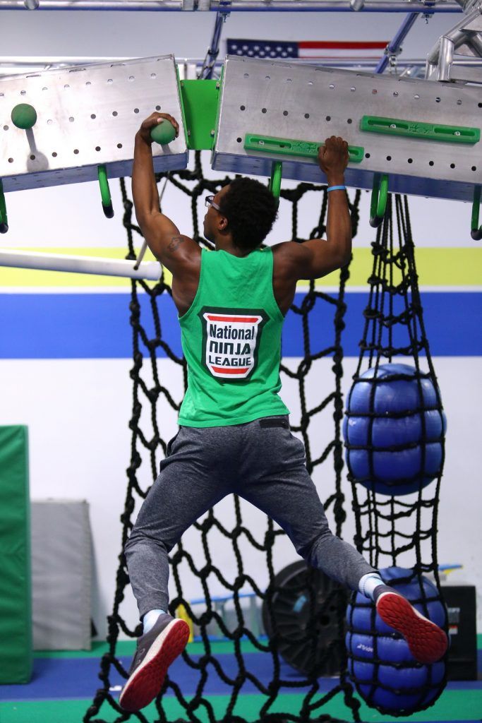 Adult in National Ninja League tank top training on rope ladder obstacle