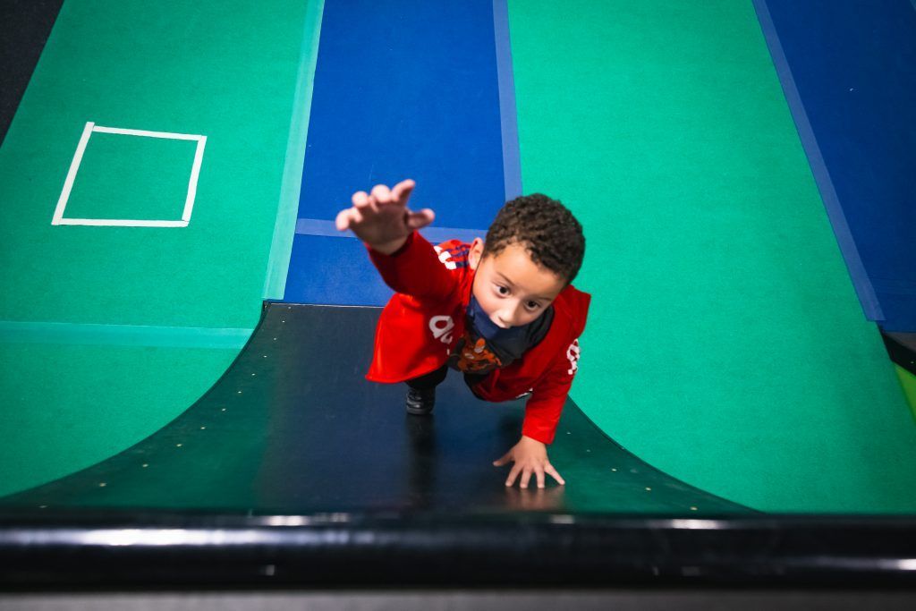 Boy in red shirt on curved warped wall obstacle on green and blue floor