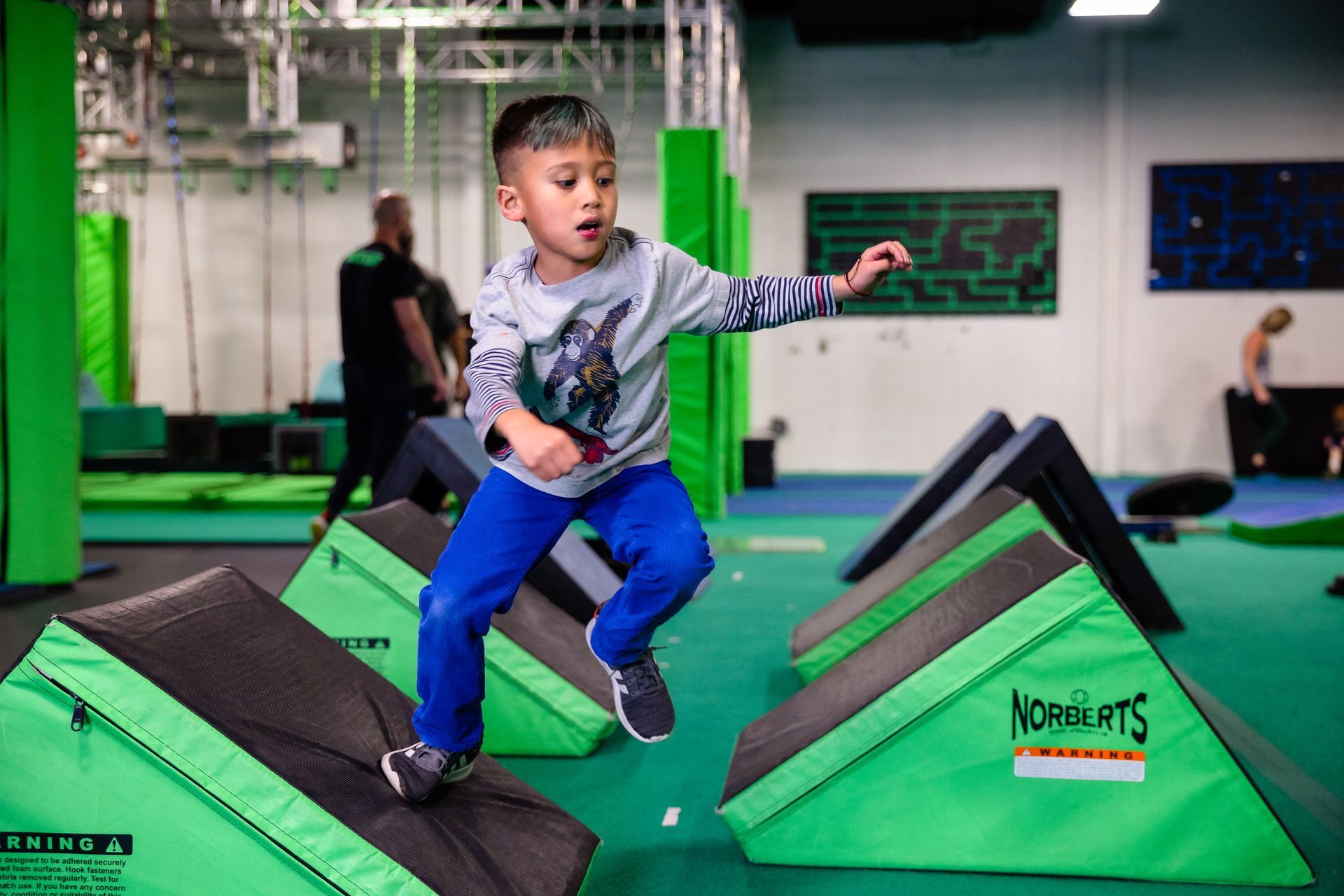 Boy jumping across angled ninja obstacles in indoor gym