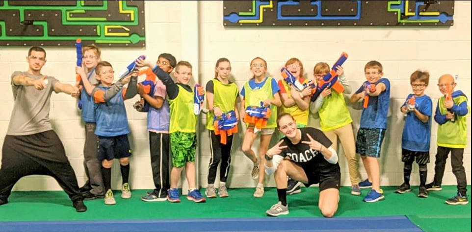 Kids in Nerf war team photo with foam guns wearing colorful jerseys