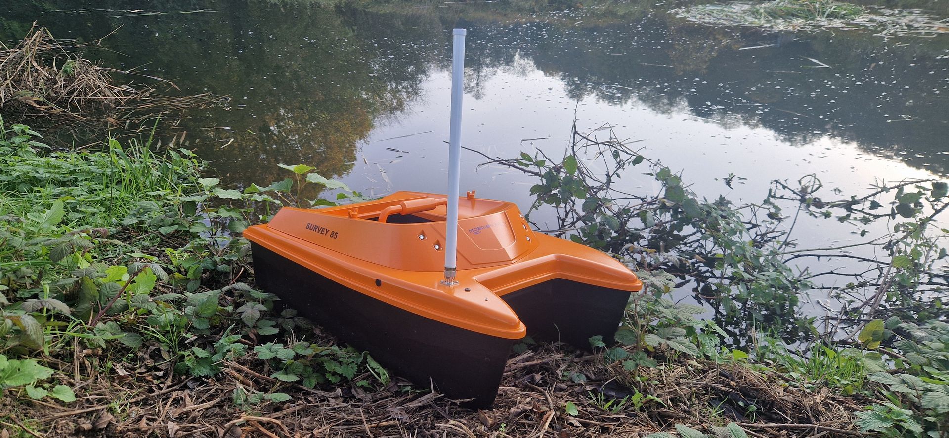 Een klein oranje bootje drijft op een meer.