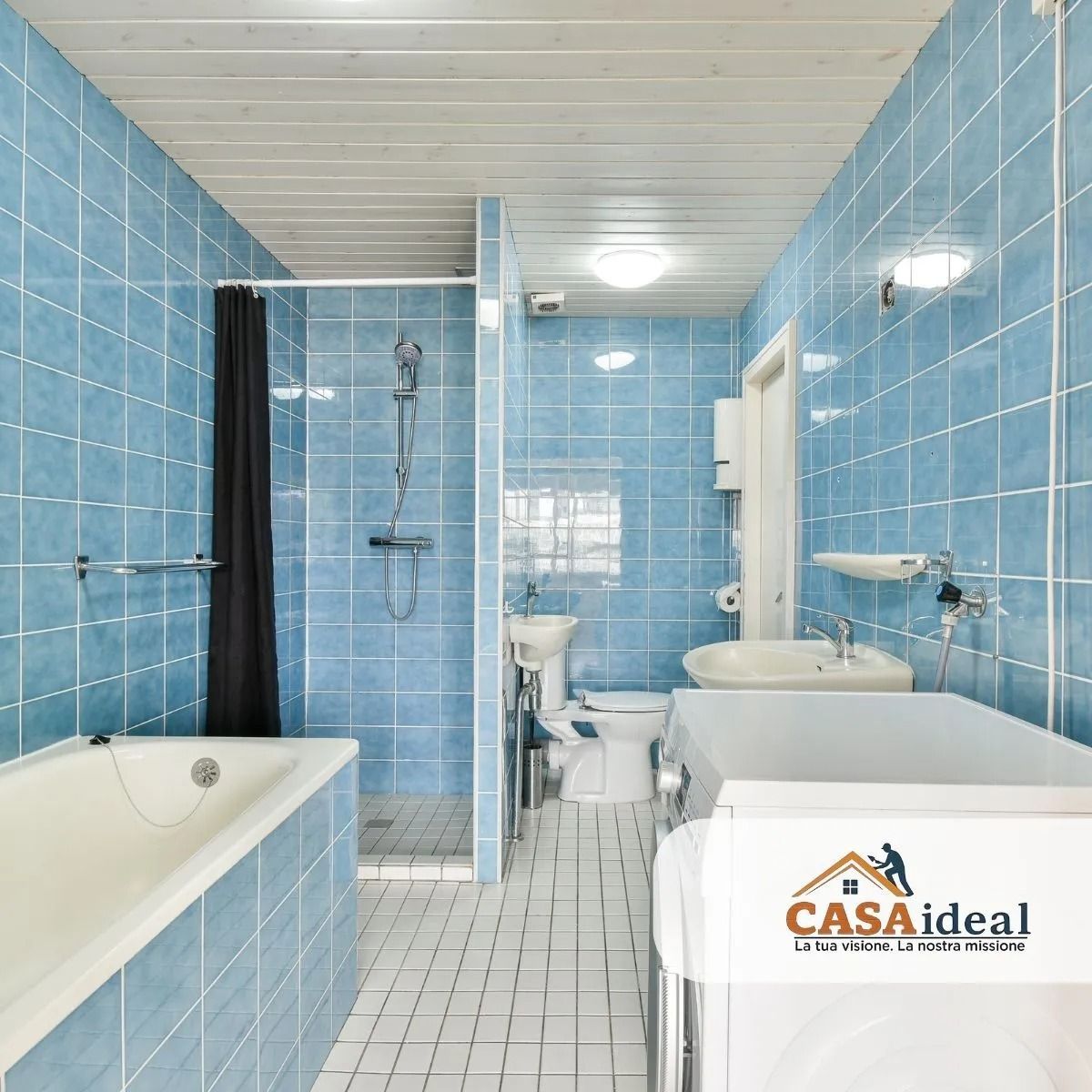 Bagno piastrellato di azzurro con vasca, doccia, lavabo e WC in uno spazio luminoso e compatto.