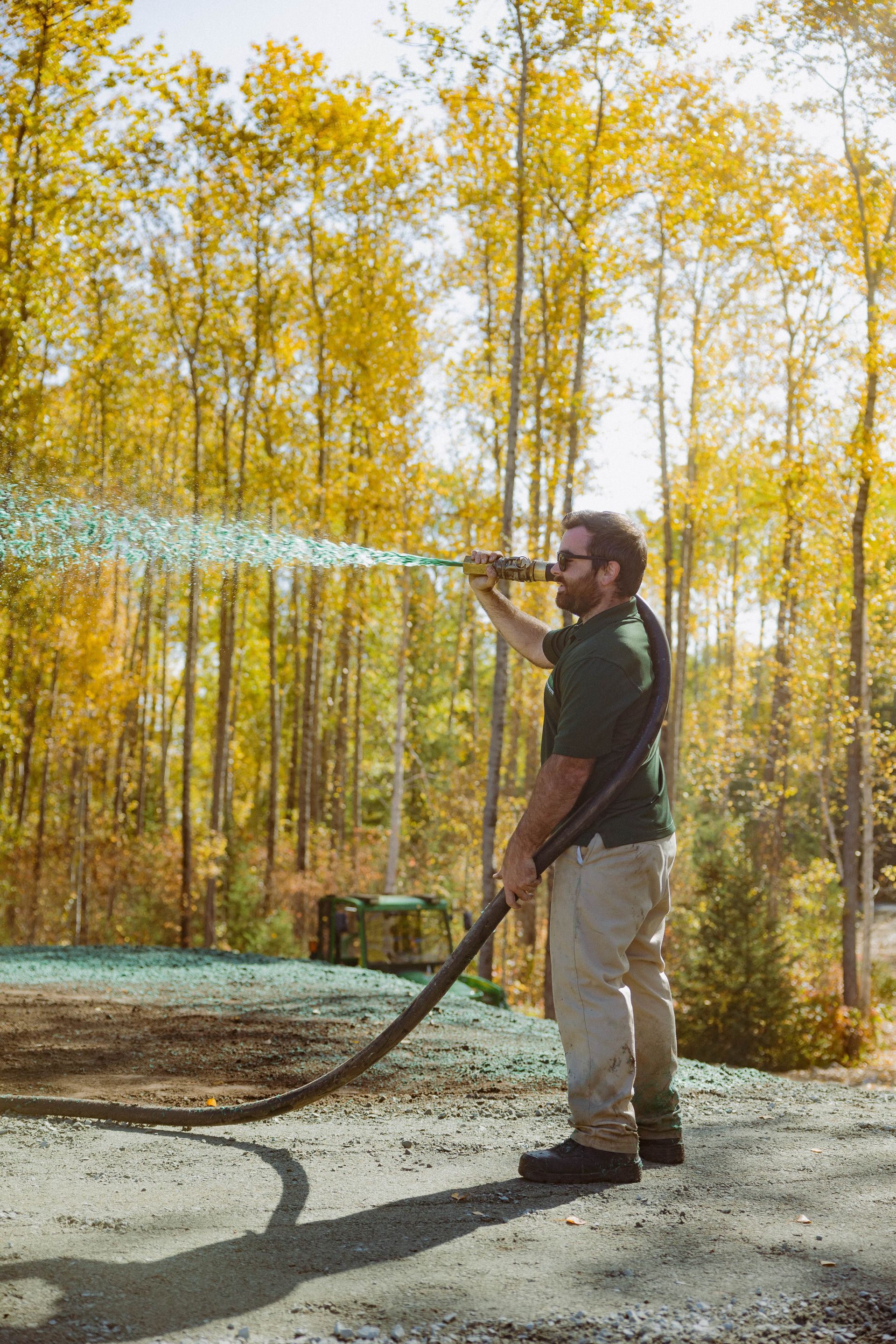 Un homme arrose les arbres avec un tuyau dans les bois.